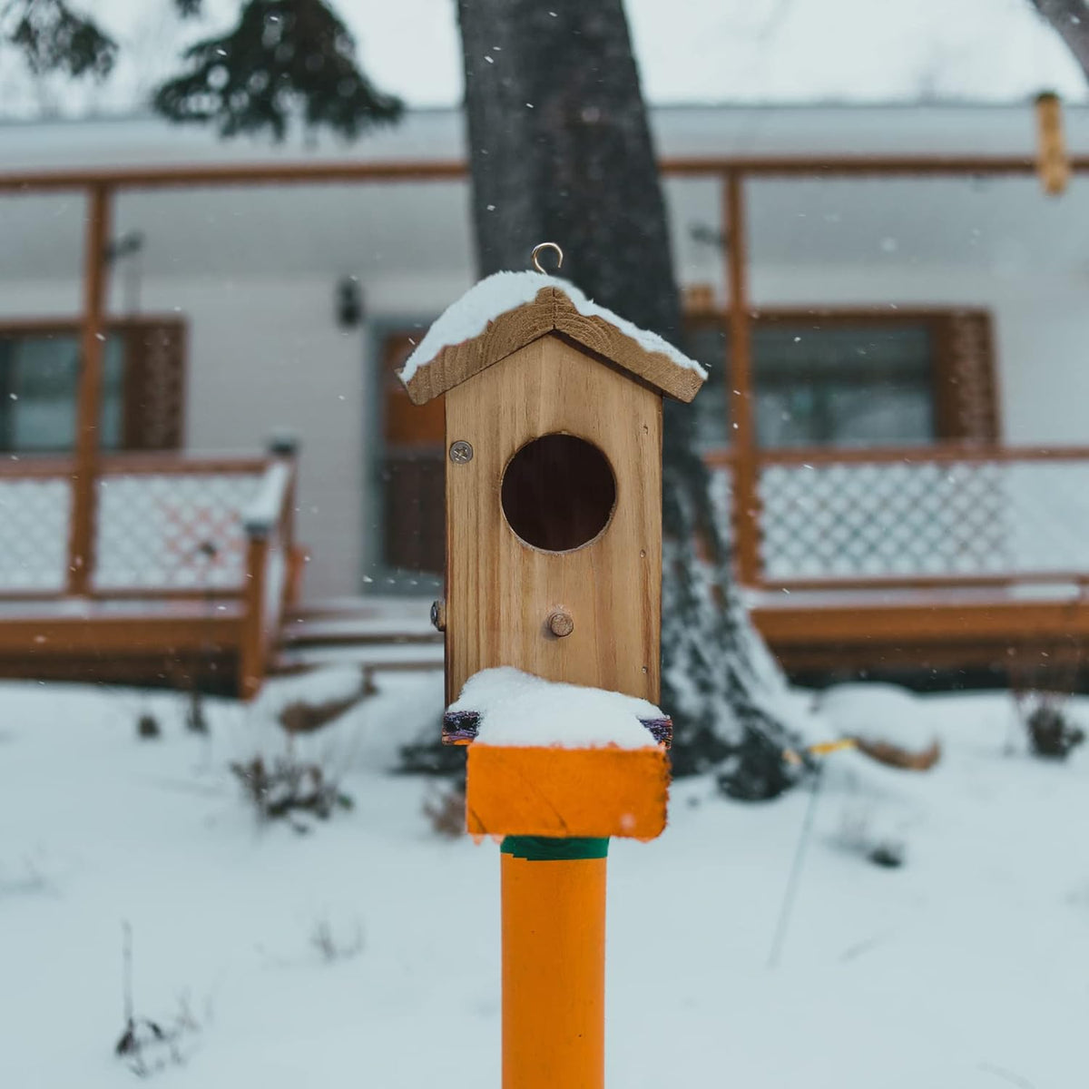 Wood hummingbird house on post with circular entrance, front latch, and hanging hook.