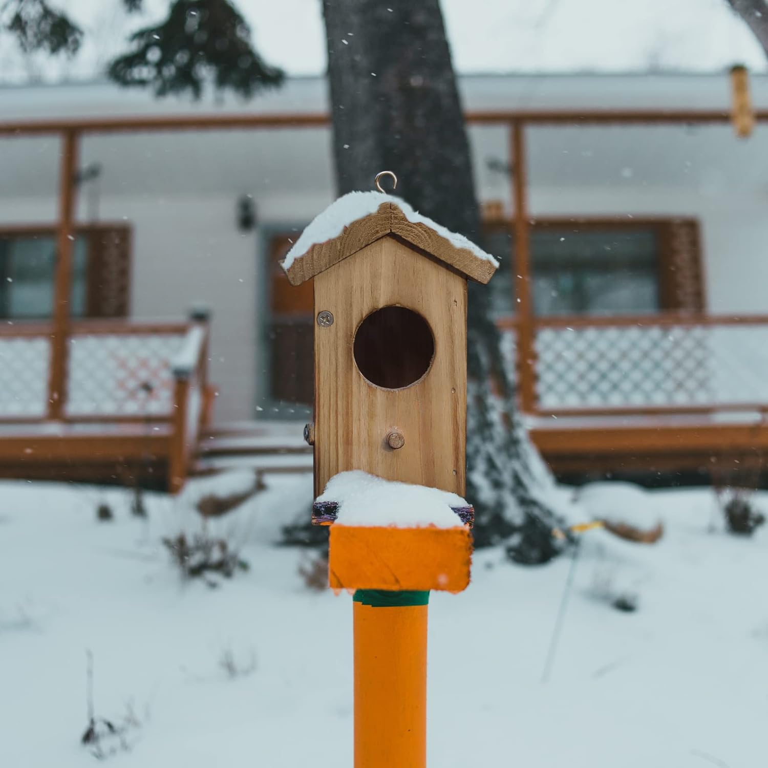 Wood hummingbird house on post with circular entrance, front latch, and hanging hook.